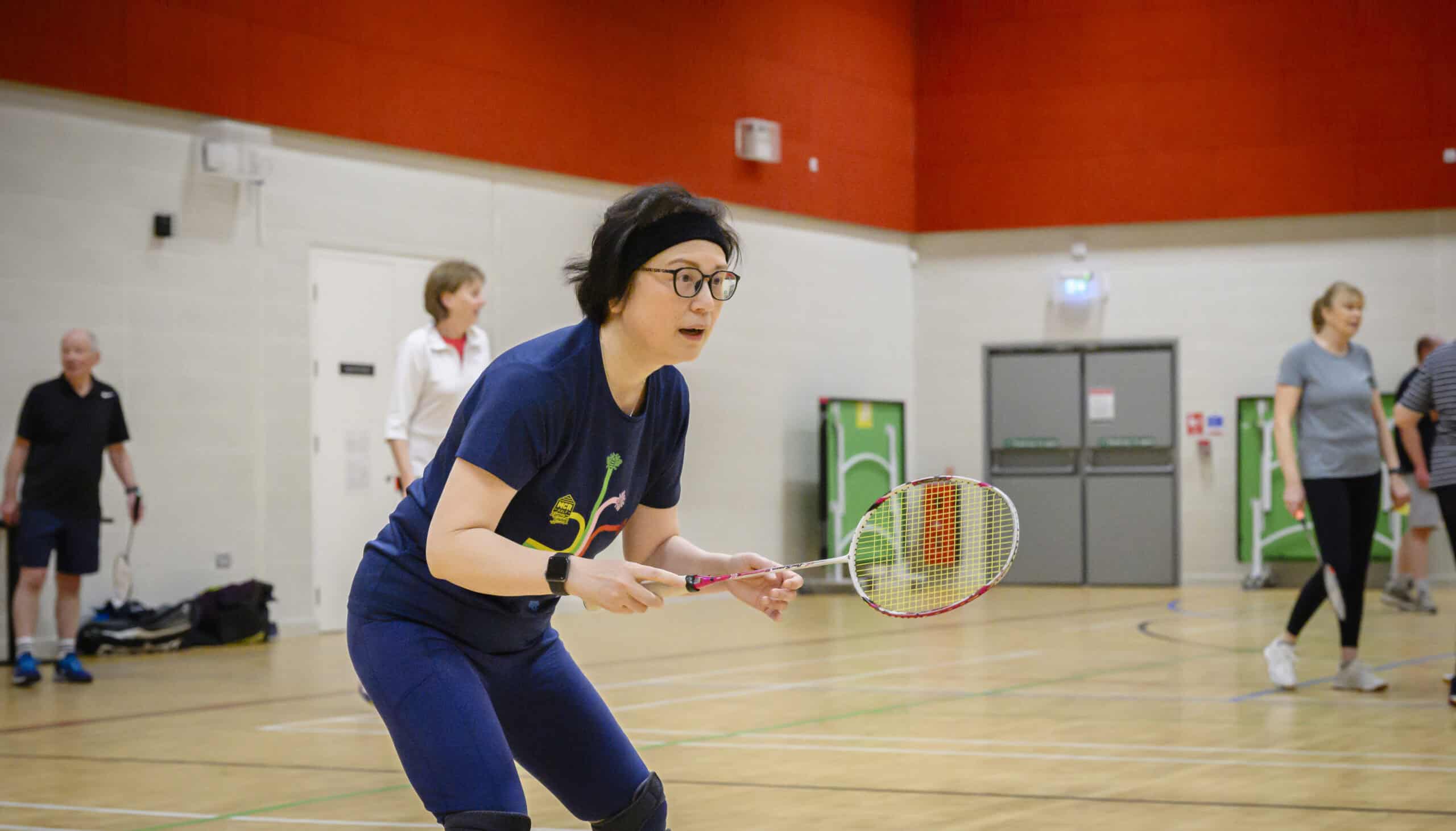 A woman playing badminton in a sports hall, holding a racket.